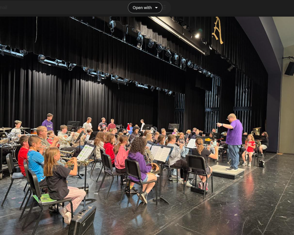 Band students sitting in chairs playing instruments on a stage
