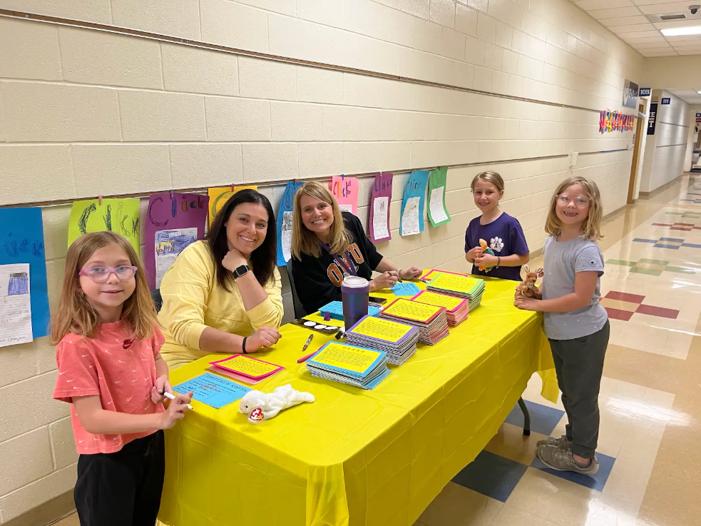 Two adults sitting at the table with three students around them