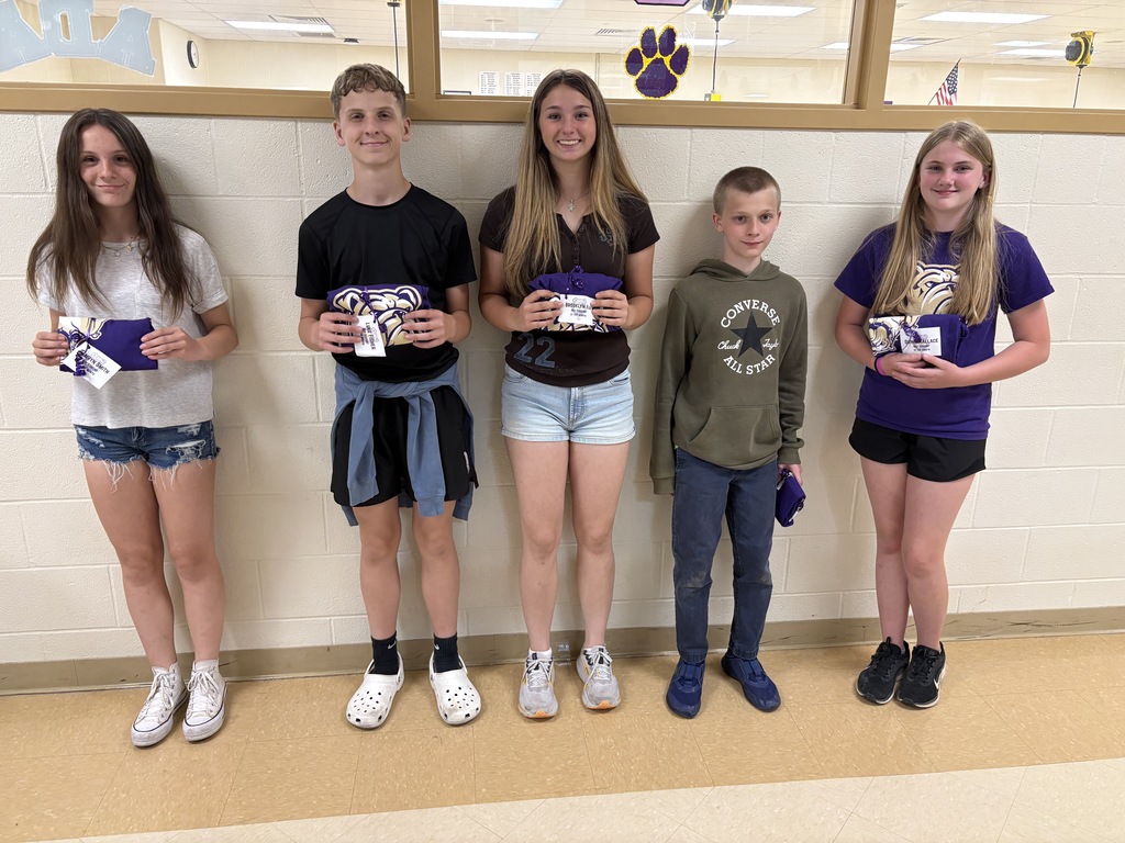 Five students holding t-shirts in front of a tan wall