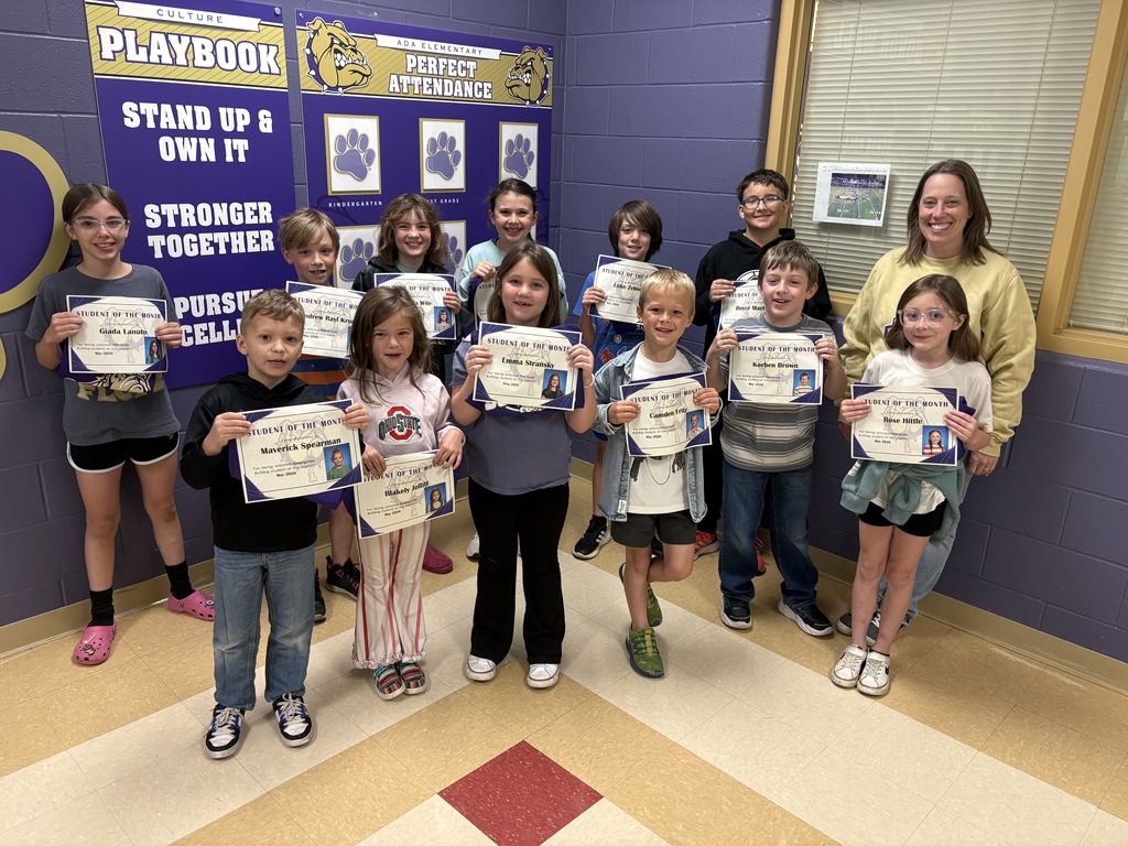 12 students holding certificates with one adult in front of a purple wall