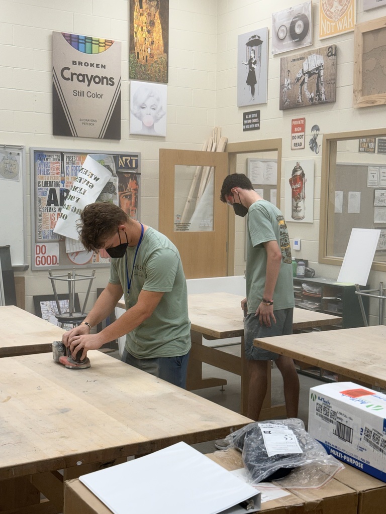 student in greenshirt sanding tables with electric sander