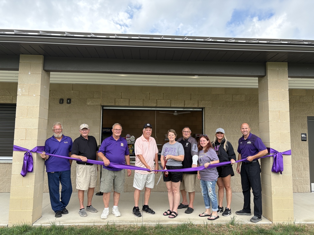Nine people holding a purple ribbon in front of concession stand with large scissor 