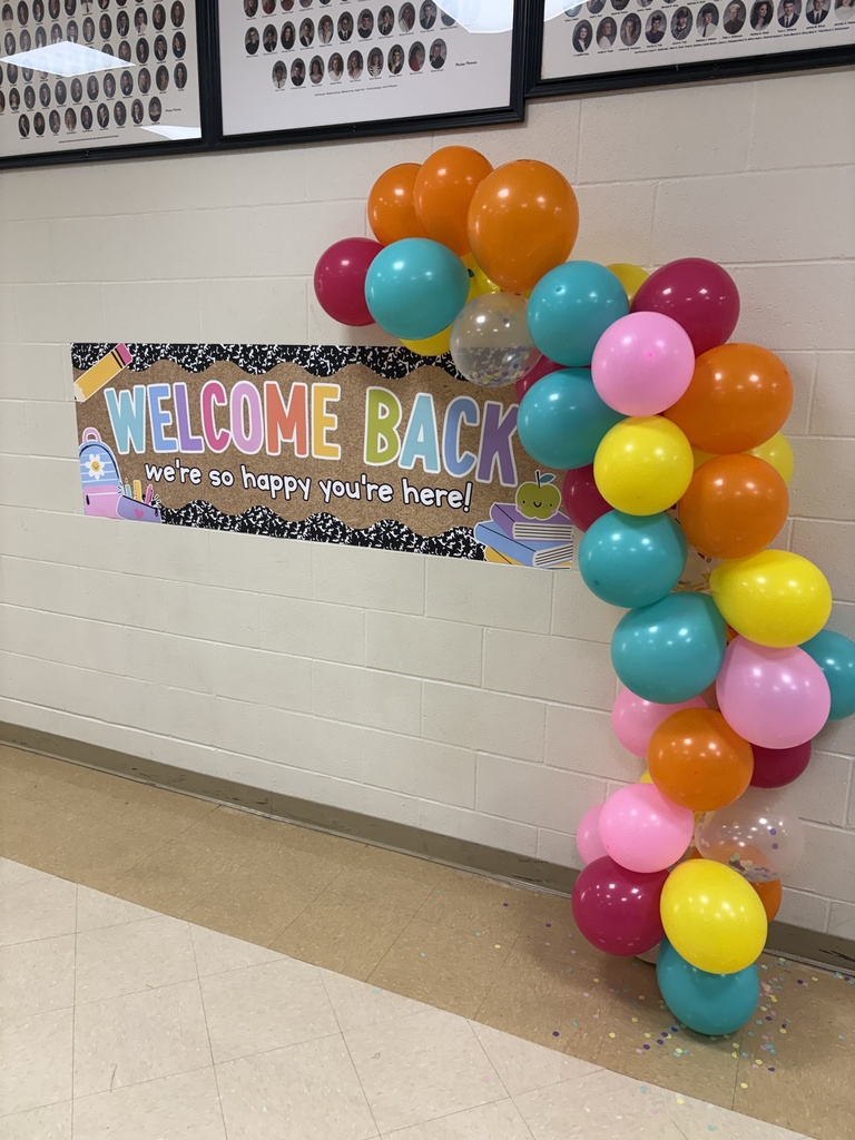 Colorful balloon arch with a welcome back sign on a beige wall