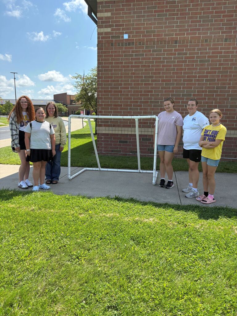 Six people standing outside around a white soccer net