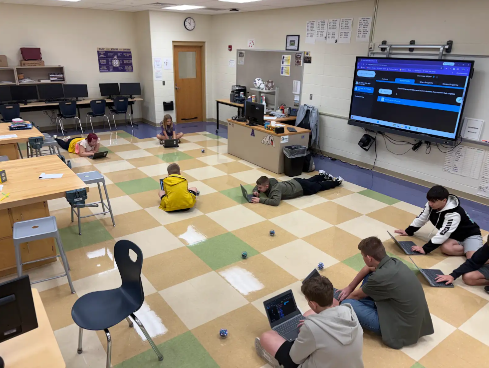 Students sitting on the floor with laptops and robots