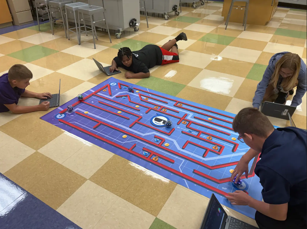 Students sitting on the floor with laptops and robots