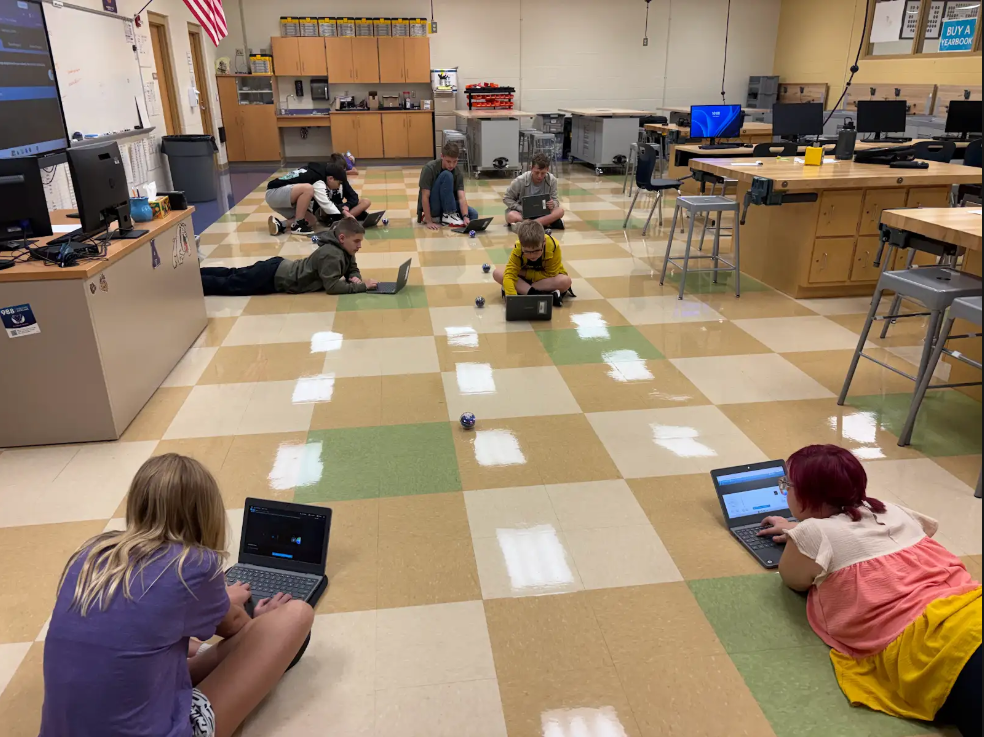 Students sitting on the floor with laptops and robots