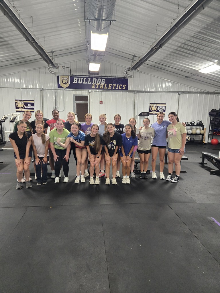 18 high school girls standing in the center of a work out room with black floor