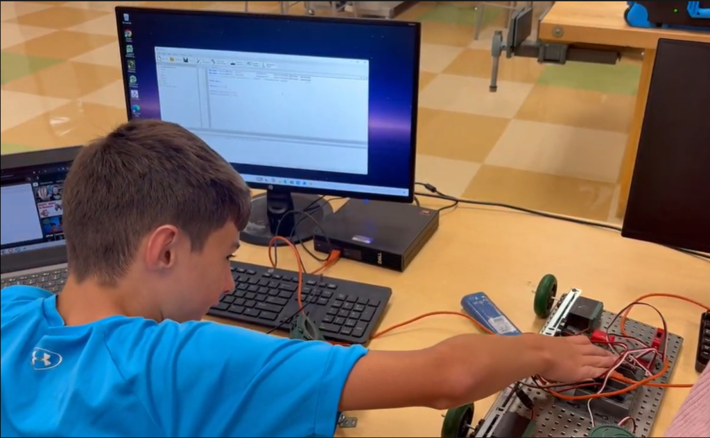 Student sitting at desk in front of computer with hand on a robot