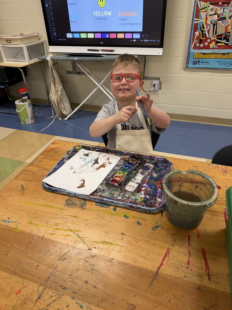 Students around a table using scissors, crayons, and paper