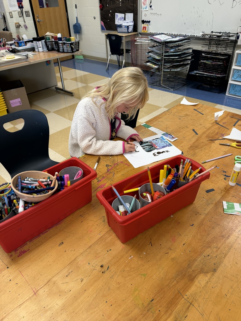 Students around a table using scissors, crayons, and paper