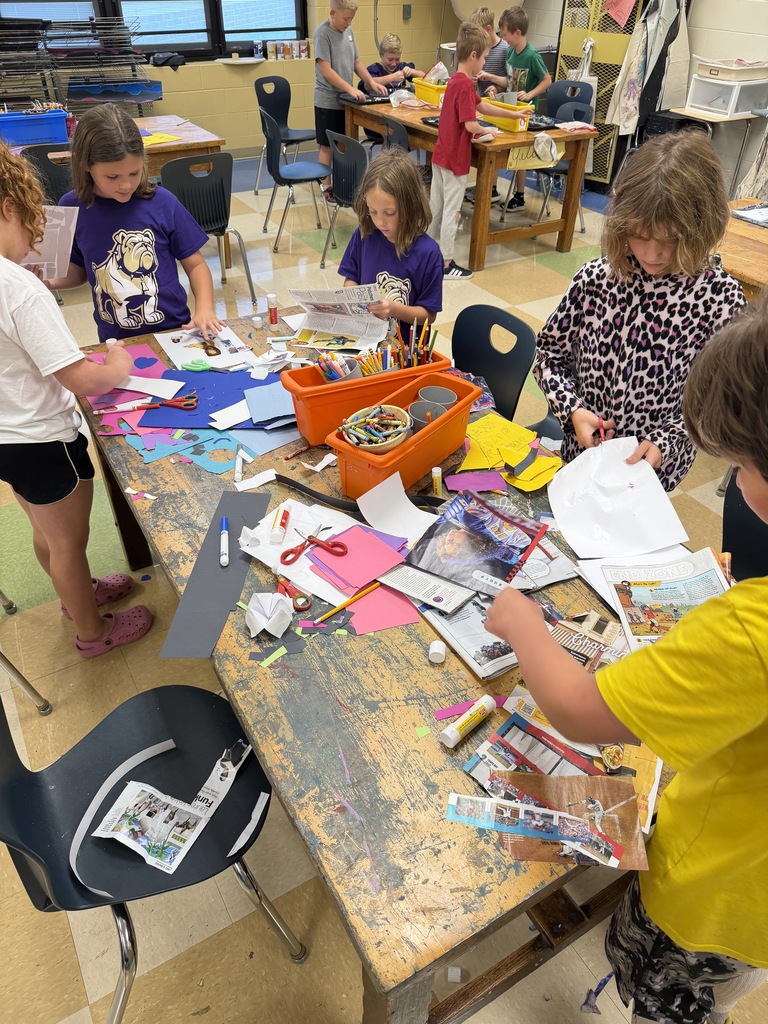 Students around a table using scissors, crayons, and paper