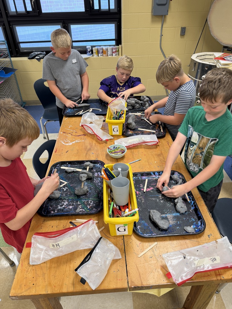 Students around a table using scissors, crayons, and paper