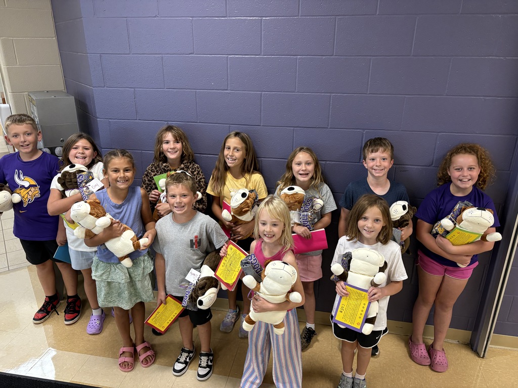 Young students standing in front of a purple wall holding stuffed dogs