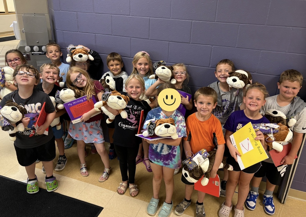 Young students standing in front of a purple wall holding stuffed dogs