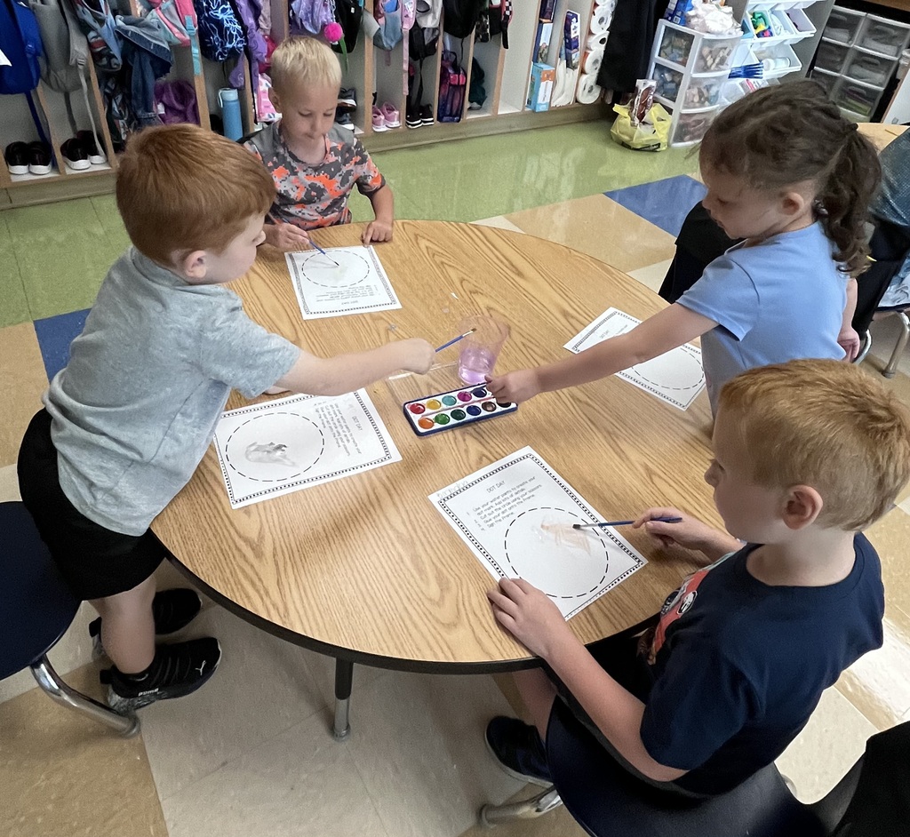 Four students sitting at a table with paper and water colors