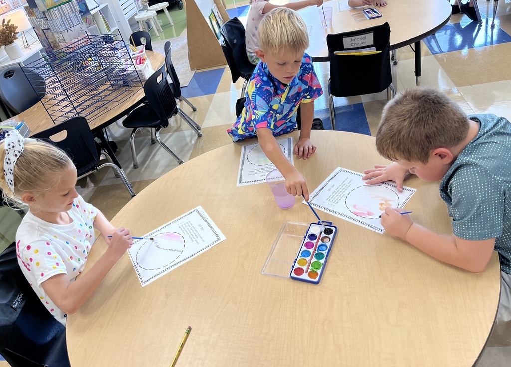 Four students sitting at a table with paper and water colors