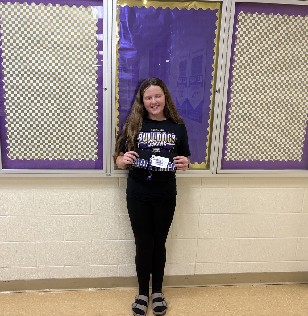 Young girl dressed in black standing in front a bulletin board holding a rolled tshirt
