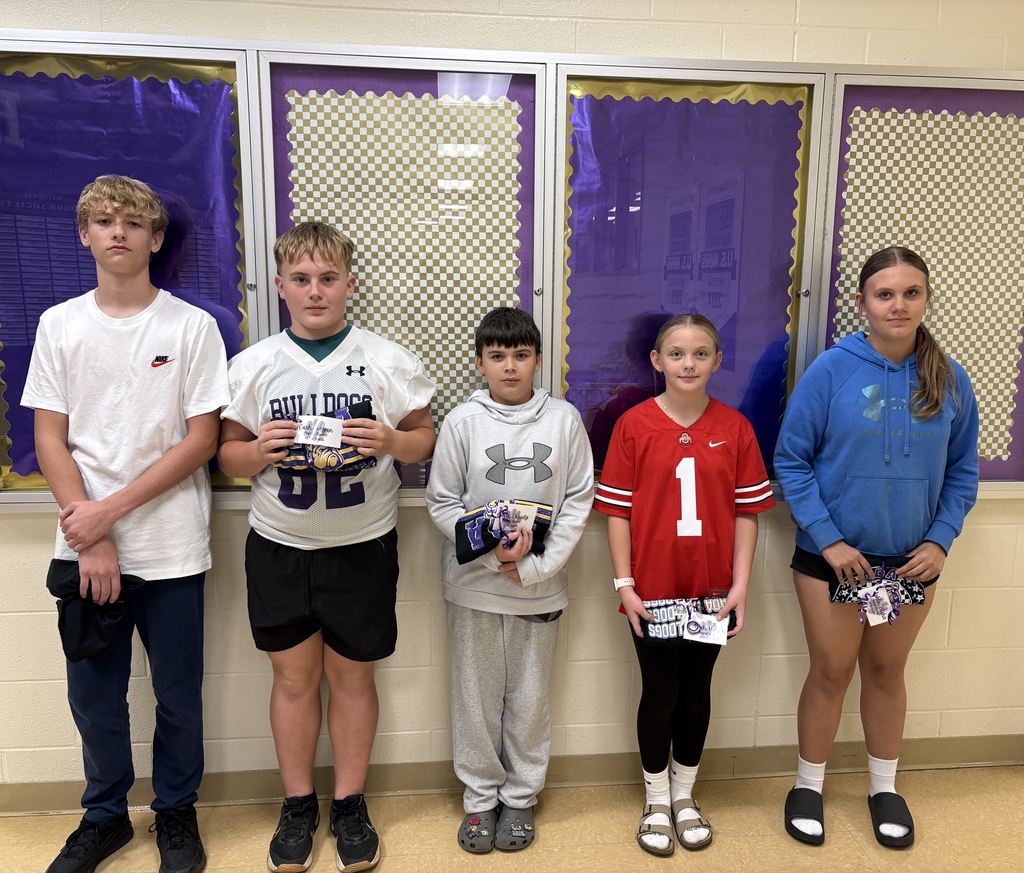 Five students standing in front a bulletin board holding a rolled tshirt