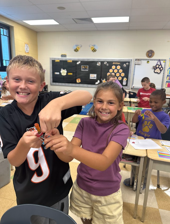 Two students using a clear plastic cup and a gummy worm standing at a desk