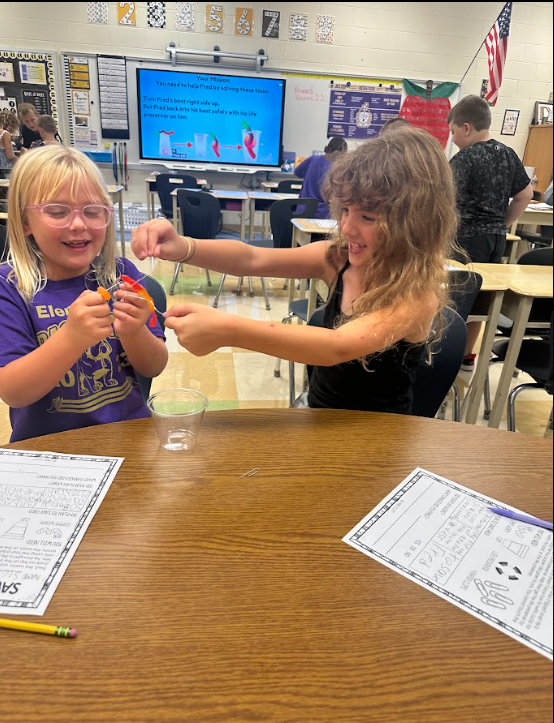 Two students using a clear plastic cup and a gummy worm standing at a desk