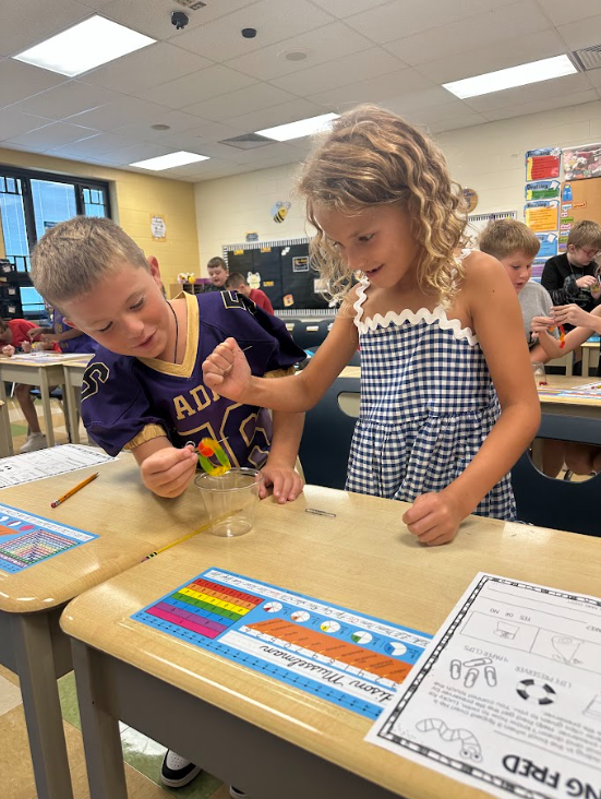 Two students using a clear plastic cup and a gummy worm standing at a desk