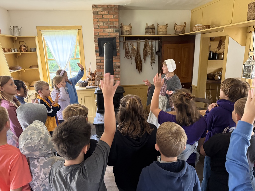 students standing around a woman with a bonnet with their hands raised