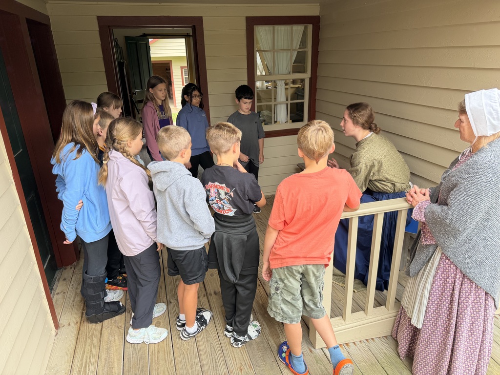 Students standing around a woman seated on a chair on a porch