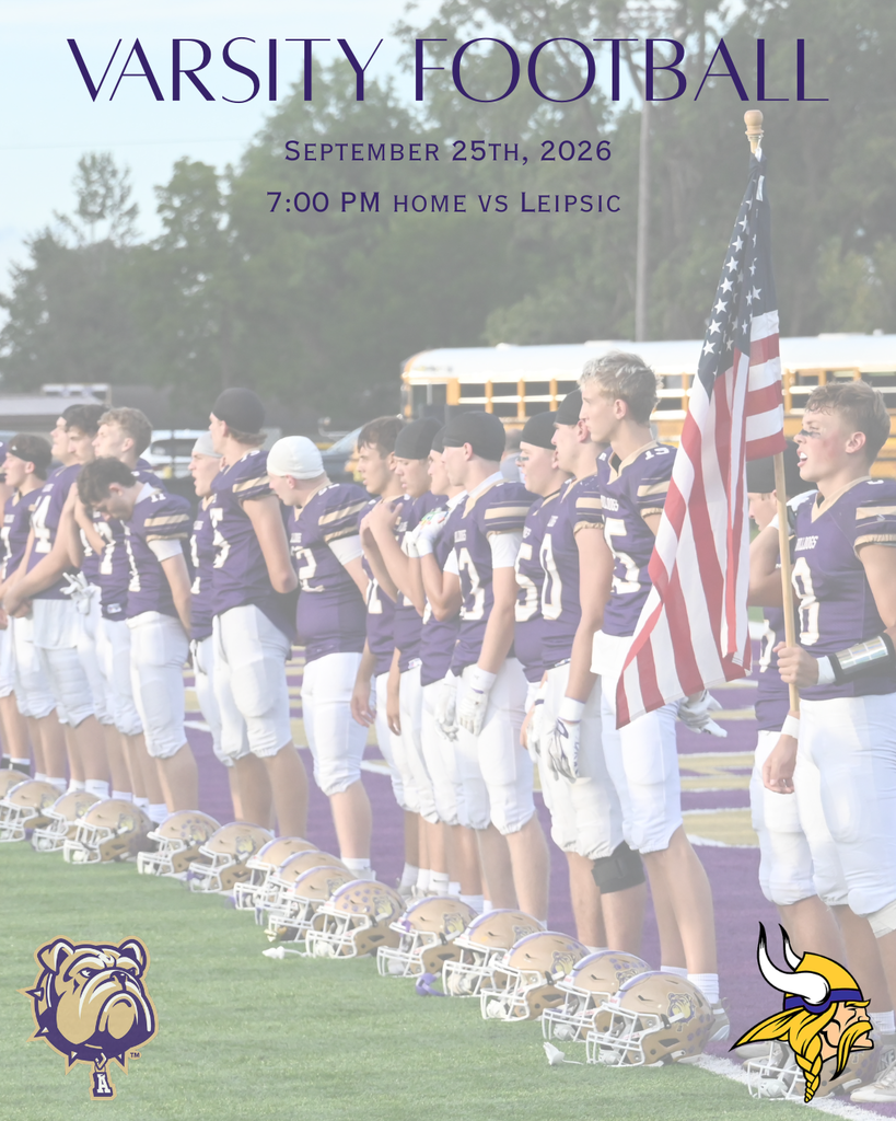 Football players standing along the football field with one student holding an American Flag