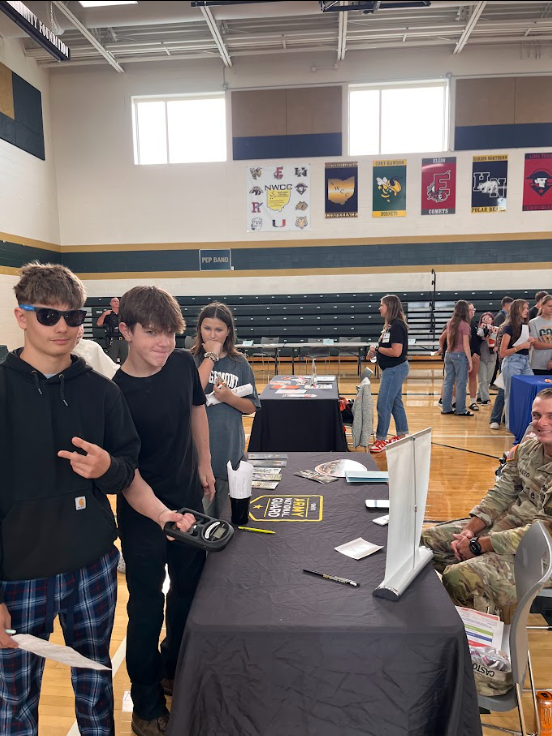 Students standign around a table talking with an adult sitting down across from them