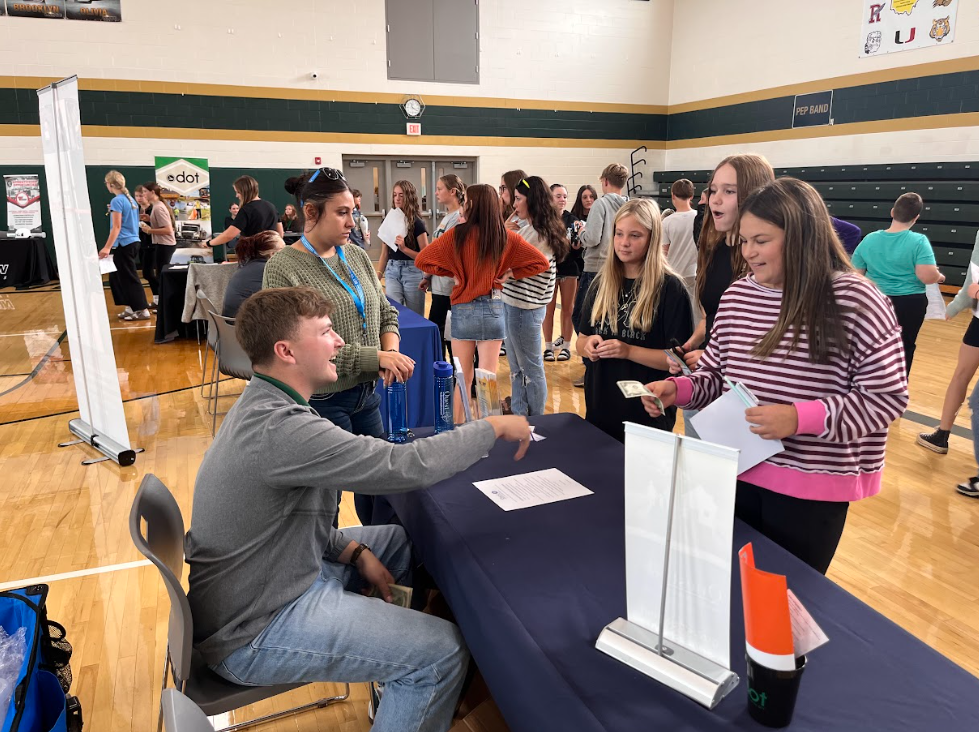 Students standign around a table talking with an adult sitting down across from them