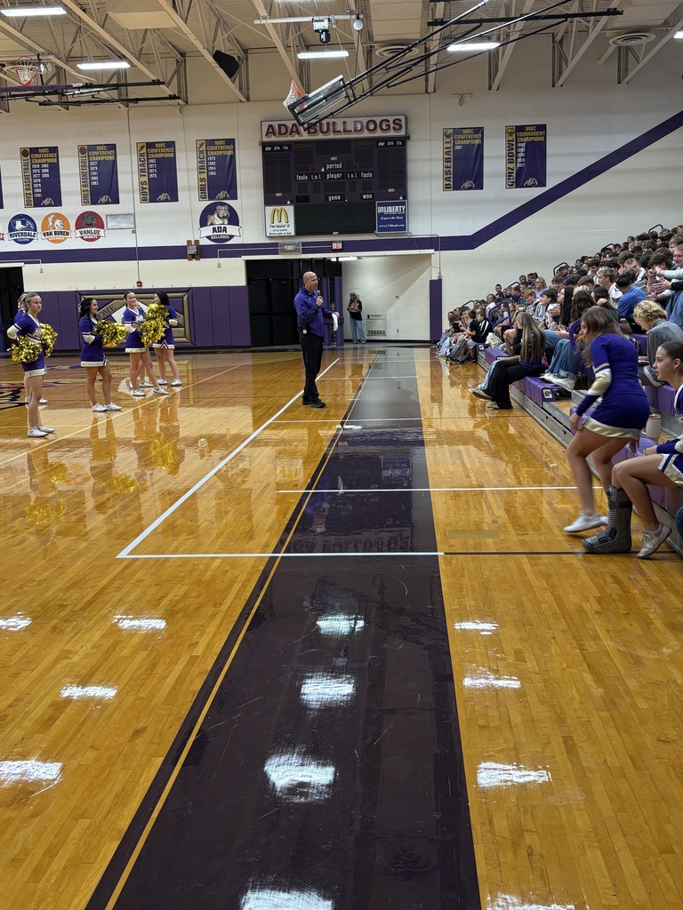 man with microphone in the gym talking to students in bleachers 