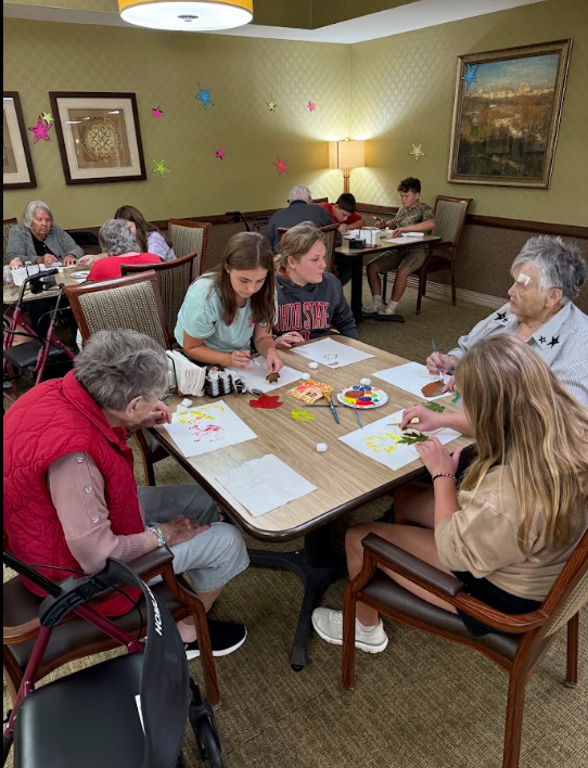 middle school students sitting at a table with elderly nursing home residents painting pictures