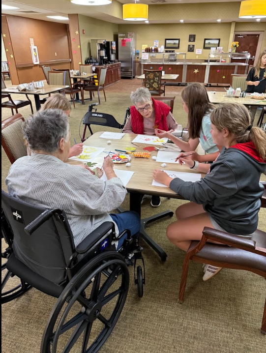 middle school students sitting at a table with elderly nursing home residents painting pictures