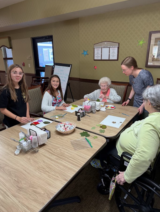 middle school students sitting at a table with elderly nursing home residents painting pictures
