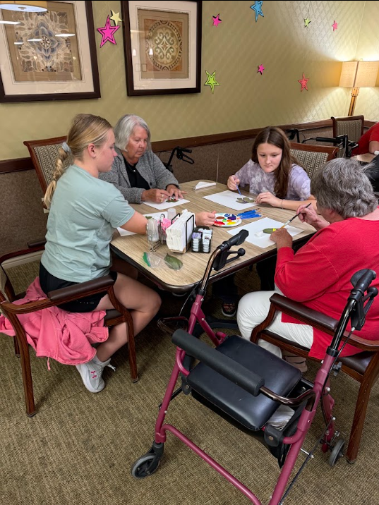 middle school students sitting at a table with elderly nursing home residents painting pictures