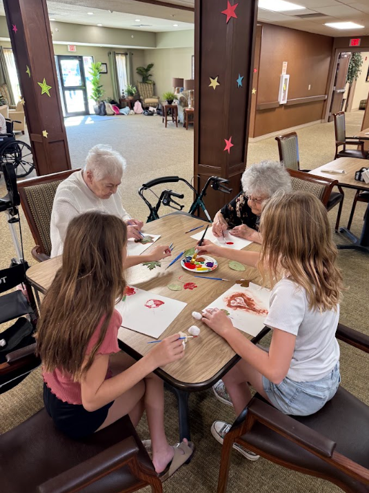 middle school students sitting at a table with elderly nursing home residents painting pictures