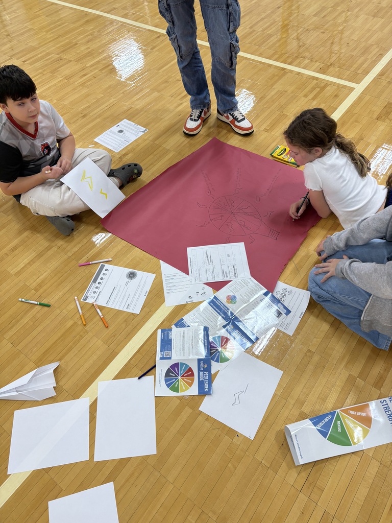 Student sitting on the gym floor working on a poster with flyers around them