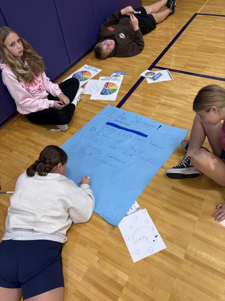 Student sitting on the gym floor working on a poster with flyers around them