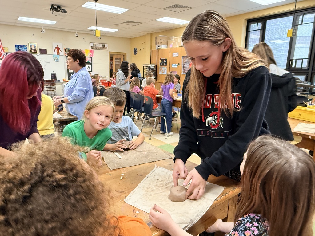 Young students crowded around a table watching a demonstration from an adult female teacher