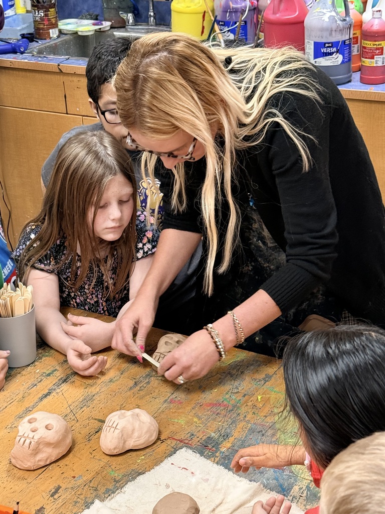 Young students crowded around a table watching a demonstration from an adult female teacher