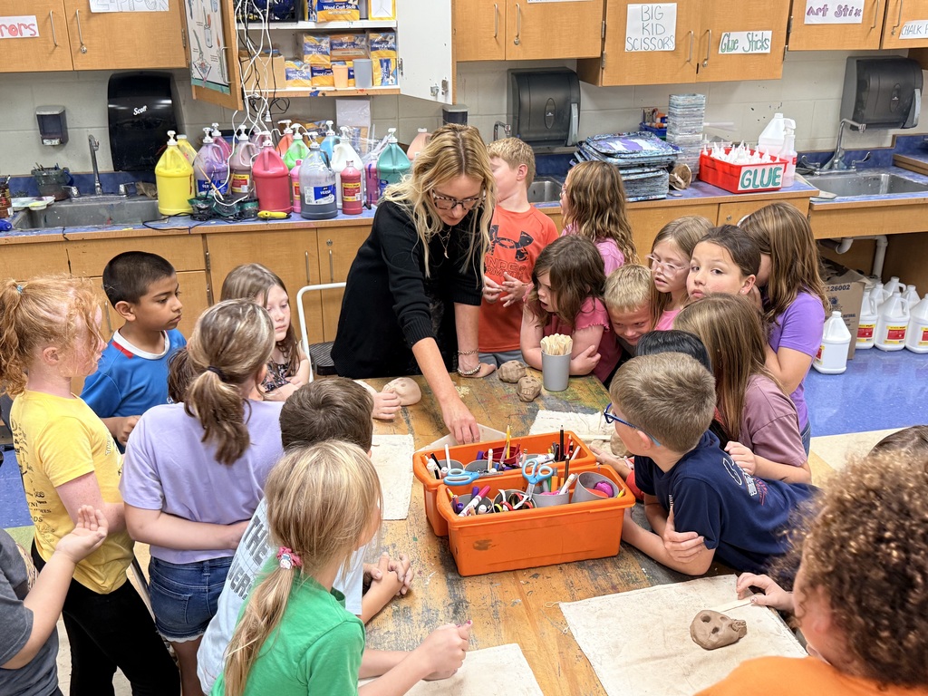 Young students crowded around a table watching a demonstration from an adult female teacher