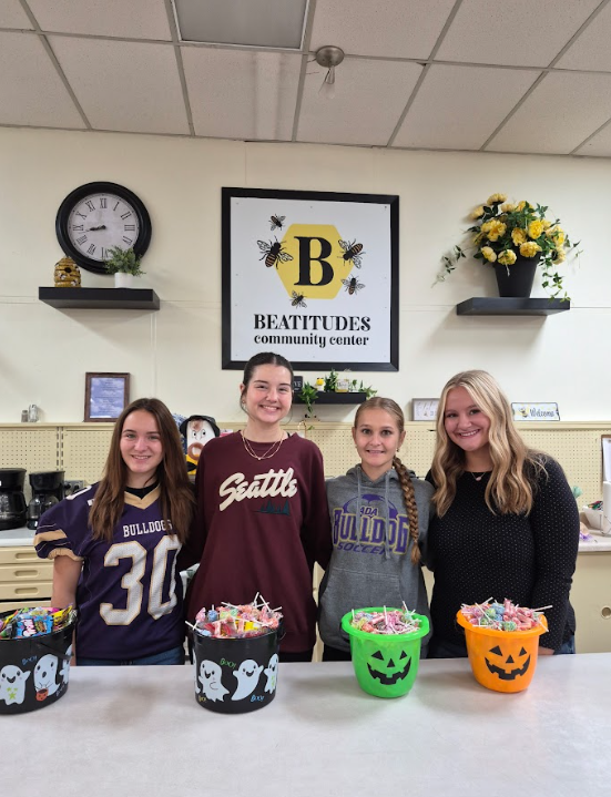four students smiling at the camera with buckets of candy in front of them