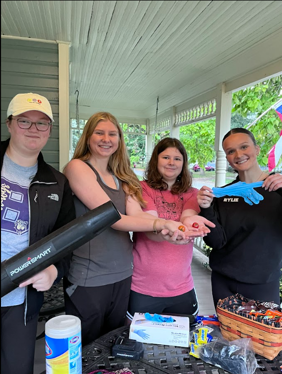 students holding cleaning supplies smiling at the camera