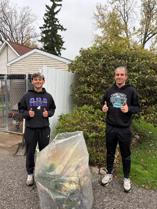 two students gathering brush and leaves into bags with thumbs up