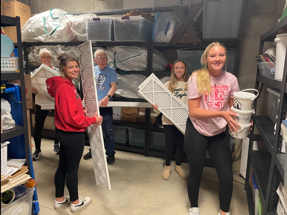 students carrying buckets and materials in a storage room