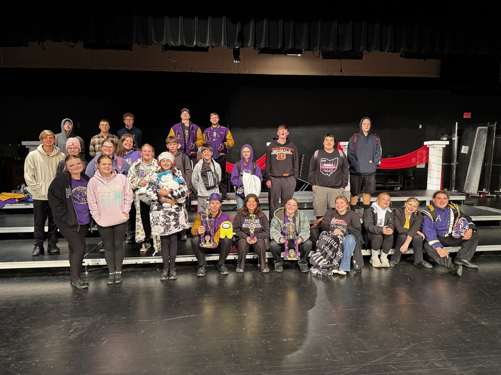 Group of high school student standing and sitting on risers in an auditorium smiling at the photographer