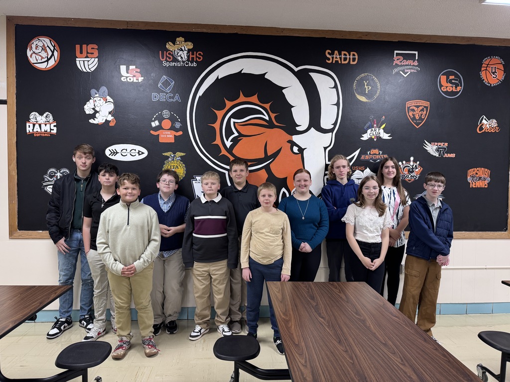 Twelve middle school students standing in front of a black wall with different graphics smiling at the photographer 