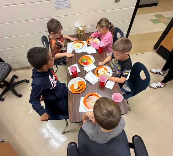 Five students sitting at a table with pumpkin plates in front of them eating quesadillas