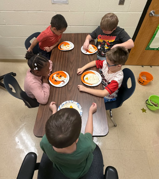 Five students sitting at a table with pumpkin plates in front of them eating quesadillas